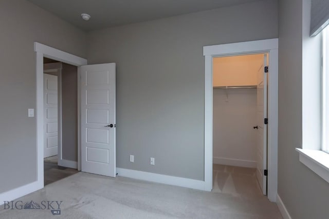 unfurnished bedroom featuring a closet, a spacious closet, carpet, and baseboards