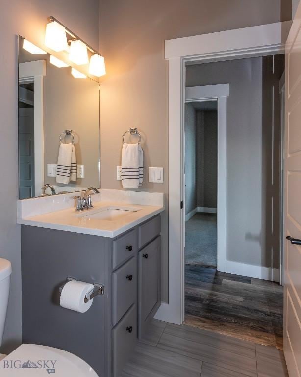 half bathroom featuring toilet, wood finished floors, vanity, and baseboards