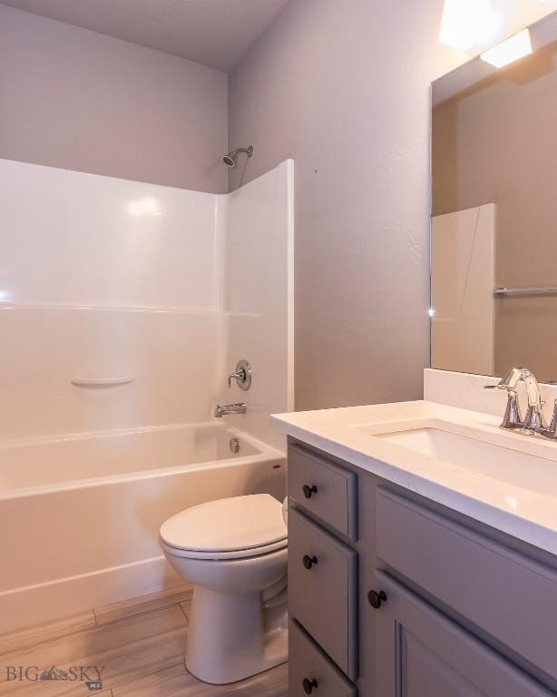 bathroom with toilet, wood finished floors, vanity, and shower / washtub combination