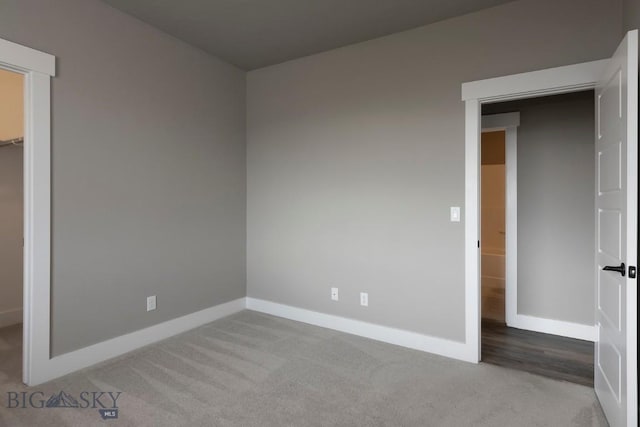 unfurnished bedroom with a closet, a walk in closet, carpet, and baseboards