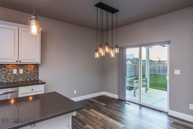 kitchen featuring white cabinetry, dark wood-type flooring, hanging light fixtures, dark stone counters, and decorative backsplash