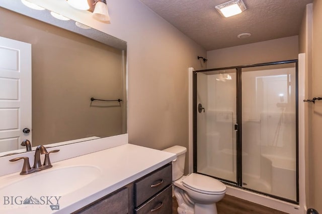 full bath featuring a textured ceiling, vanity, toilet, wood finished floors, and a stall shower