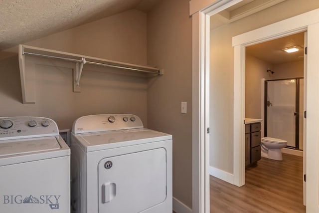 washroom with baseboards, light wood-type flooring, a textured ceiling, washer and clothes dryer, and laundry area