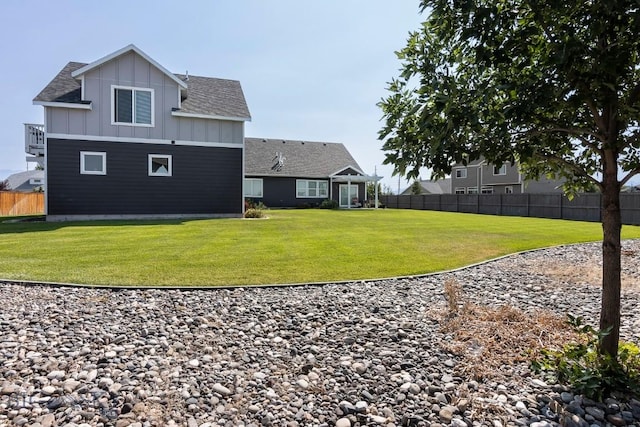 rear view of property featuring board and batten siding, roof with shingles, a yard, and fence