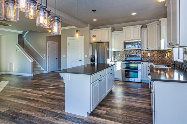 2133 Stewart Loop, Bozeman, MT 59718 - kitchen with appliances with stainless steel finishes, dark countertops, dark wood-type flooring, a kitchen island, and backsplash