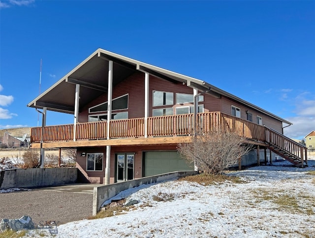 snow covered rear of property featuring a garage and a wooden deck