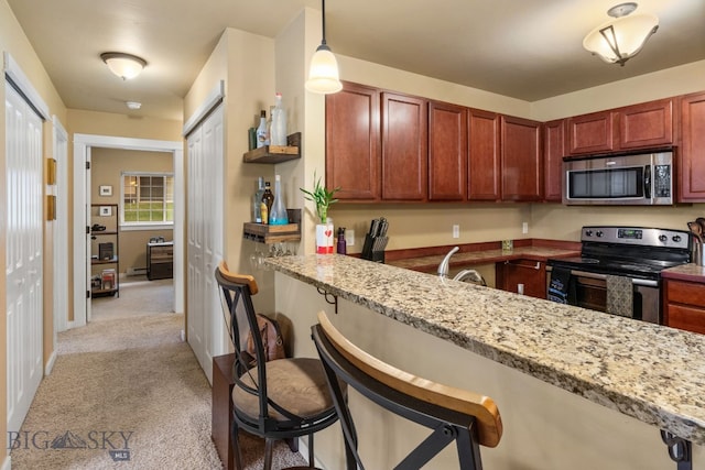 kitchen featuring light carpet, appliances with stainless steel finishes, light stone counters, and a kitchen breakfast bar