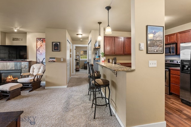 kitchen with hanging light fixtures, light stone counters, a breakfast bar area, appliances with stainless steel finishes, and hardwood / wood-style flooring