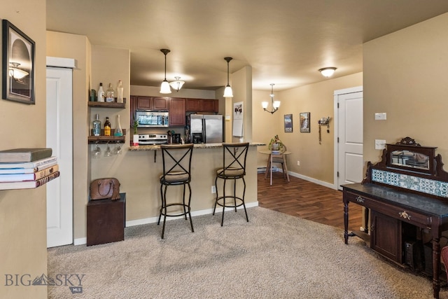 kitchen with kitchen peninsula, appliances with stainless steel finishes, a kitchen breakfast bar, light hardwood / wood-style floors, and hanging light fixtures