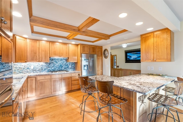 kitchen featuring light stone countertops, stainless steel appliances, a kitchen breakfast bar, light hardwood / wood-style flooring, and kitchen peninsula