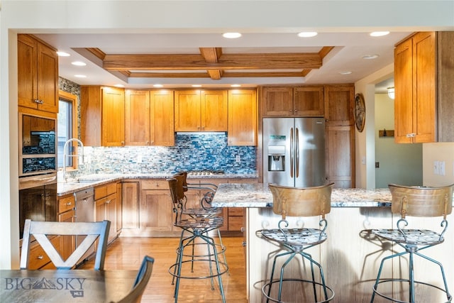 kitchen with light stone countertops, a tray ceiling, a breakfast bar, appliances with stainless steel finishes, and light wood-type flooring