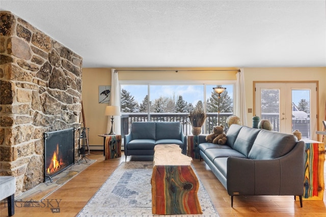 living room with a textured ceiling, light wood-type flooring, a stone fireplace, and plenty of natural light