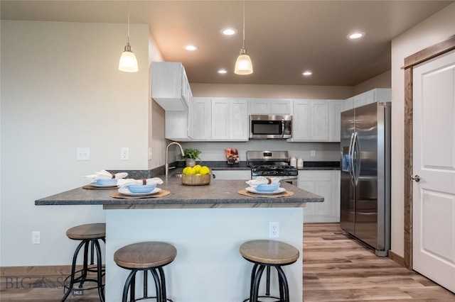 kitchen featuring kitchen peninsula, a kitchen breakfast bar, stainless steel appliances, and white cabinetry