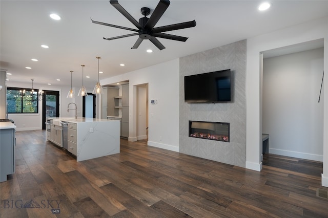 kitchen featuring dark wood-type flooring, a spacious island, hanging light fixtures, light stone countertops, and a fireplace