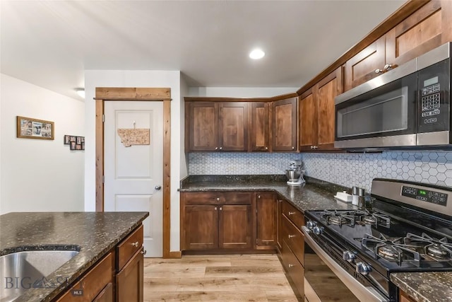 kitchen featuring appliances with stainless steel finishes, sink, backsplash, dark stone counters, and light hardwood / wood-style floors