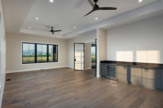 unfurnished living room featuring wood-type flooring, a tray ceiling, beverage cooler, and ceiling fan