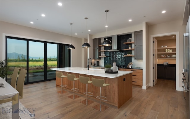 kitchen featuring hanging light fixtures, light hardwood / wood-style flooring, range hood, a large island, and light stone counters