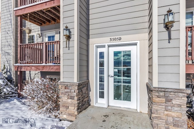 snow covered property entrance featuring a balcony