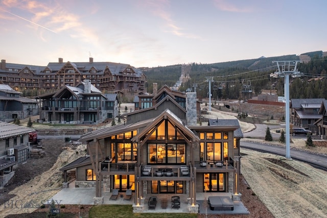 back house at dusk featuring a balcony and a patio