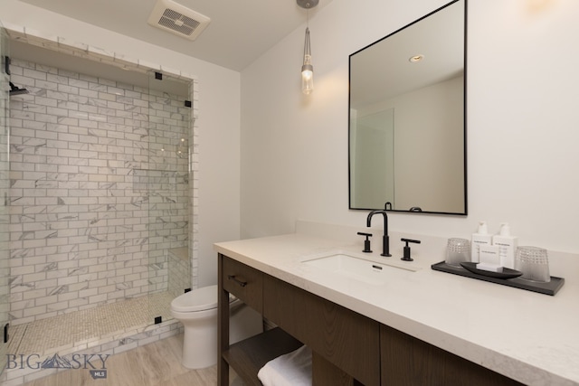 bathroom with tiled shower, vanity, hardwood / wood-style flooring, and toilet