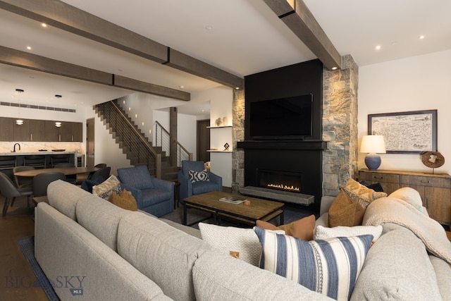 living room featuring beamed ceiling, a stone fireplace, wood-type flooring, and sink