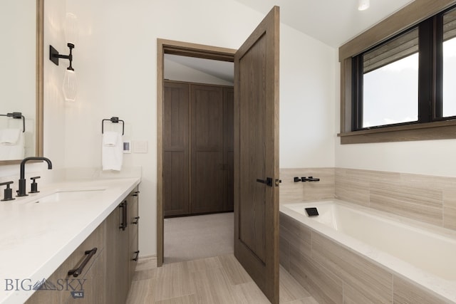 bathroom featuring tile patterned flooring, vanity, a relaxing tiled tub, and vaulted ceiling