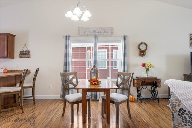 dining space with hardwood / wood-style flooring, a notable chandelier, and vaulted ceiling