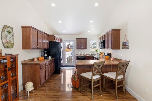 kitchen with black appliances, kitchen peninsula, dark wood-type flooring, and vaulted ceiling