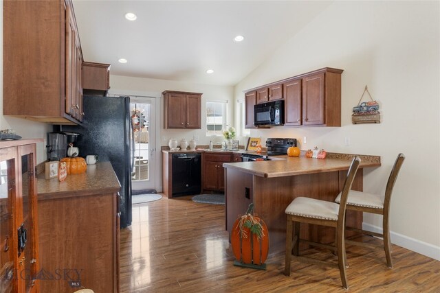 kitchen with dark hardwood / wood-style floors, kitchen peninsula, lofted ceiling, a kitchen bar, and black appliances