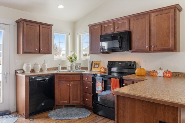 kitchen featuring sink, black appliances, vaulted ceiling, and light hardwood / wood-style floors