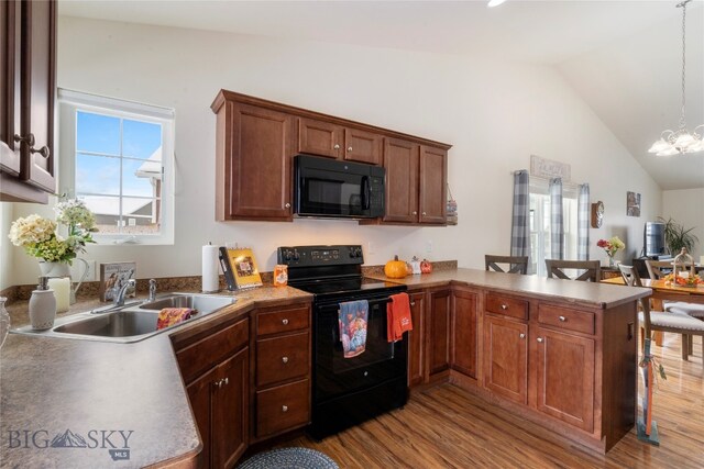 kitchen featuring sink, light hardwood / wood-style floors, decorative light fixtures, lofted ceiling, and black appliances