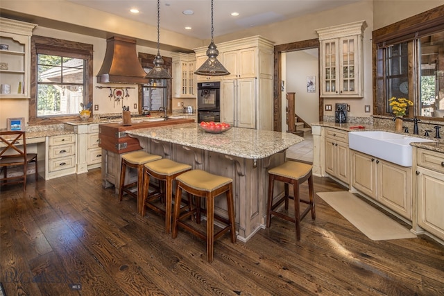 kitchen featuring custom exhaust hood, dark wood-type flooring, sink, black double oven, and a kitchen island