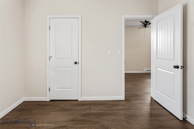 spare room featuring a baseboard heating unit, ceiling fan, and dark wood-type flooring