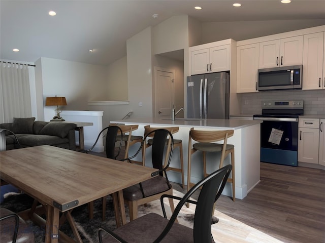 kitchen with white cabinetry, lofted ceiling, decorative backsplash, a center island with sink, and appliances with stainless steel finishes