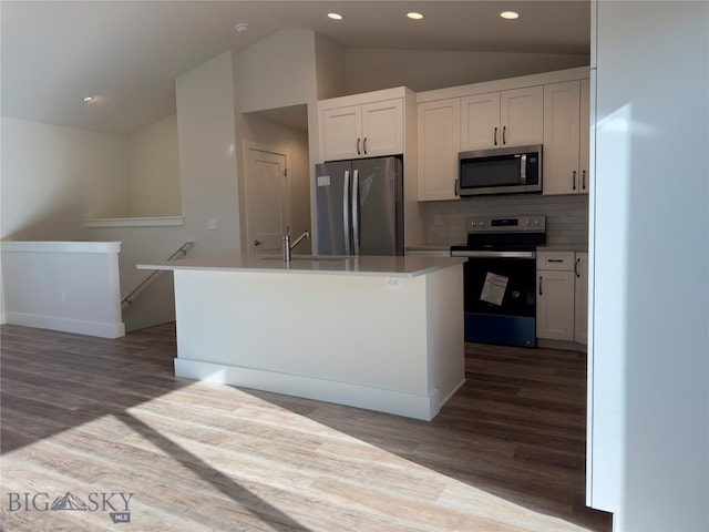 kitchen with appliances with stainless steel finishes, white cabinetry, vaulted ceiling, and an island with sink