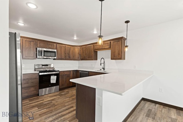 kitchen featuring kitchen peninsula, stainless steel appliances, hanging light fixtures, and dark wood-type flooring