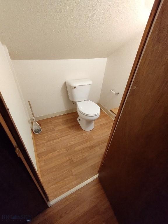 bathroom featuring a textured ceiling, hardwood / wood-style flooring, toilet, and lofted ceiling