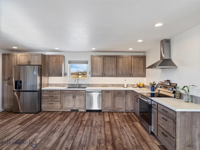 kitchen with wall chimney exhaust hood, stainless steel appliances, dark wood-style floors, a sink, and light countertops