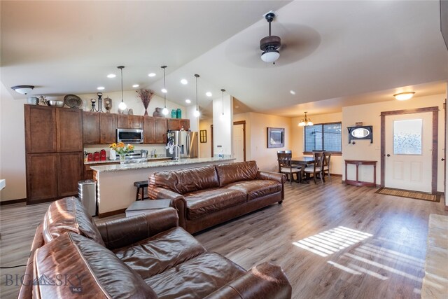 living room featuring ceiling fan with notable chandelier, light hardwood / wood-style flooring, and vaulted ceiling