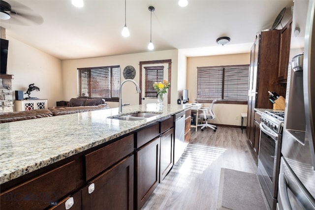 kitchen with light stone countertops, appliances with stainless steel finishes, light wood-type flooring, sink, and decorative light fixtures