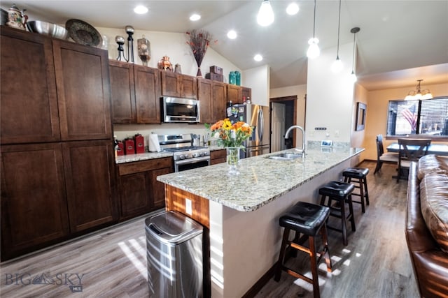 kitchen featuring sink, hanging light fixtures, stainless steel appliances, light hardwood / wood-style flooring, and a kitchen bar