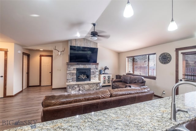 living room with ceiling fan, sink, wood-type flooring, vaulted ceiling, and a fireplace