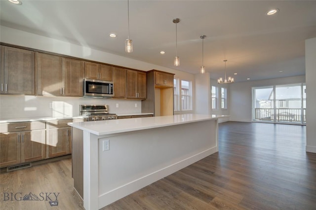 kitchen with hardwood / wood-style floors, a center island, an inviting chandelier, hanging light fixtures, and stainless steel appliances