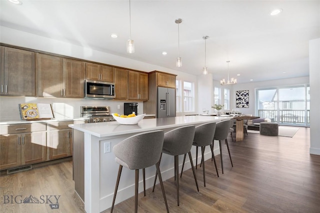 kitchen featuring a center island, wood-type flooring, decorative light fixtures, a breakfast bar area, and appliances with stainless steel finishes