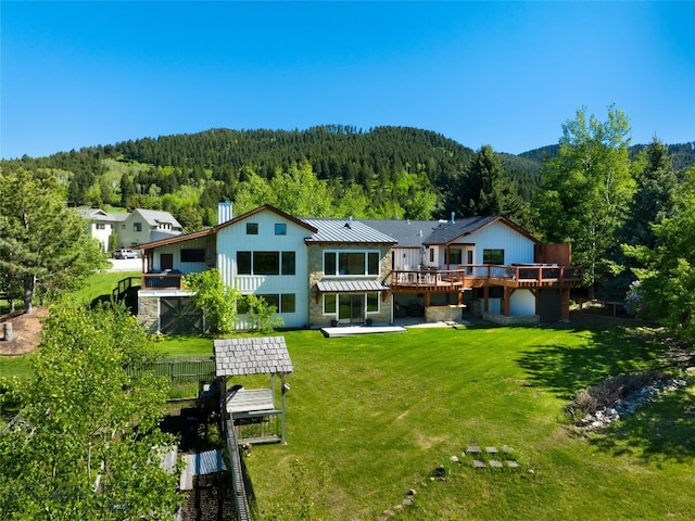 rear view of property with a lawn, a wooden deck, and a patio