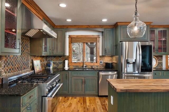 kitchen featuring wall chimney exhaust hood, backsplash, decorative light fixtures, appliances with stainless steel finishes, and light wood-type flooring