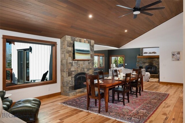 dining space featuring vaulted ceiling, ceiling fan, light wood-type flooring, a fireplace, and wood ceiling