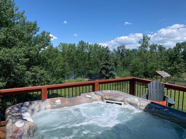 deck featuring a lawn, a trampoline, and a hot tub