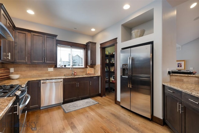 kitchen with sink, appliances with stainless steel finishes, dark brown cabinets, light stone counters, and tasteful backsplash