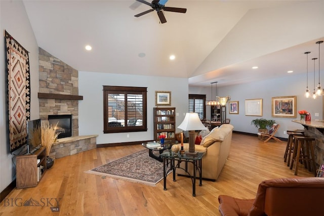 living room featuring high vaulted ceiling, a stone fireplace, ceiling fan with notable chandelier, and light hardwood / wood-style floors